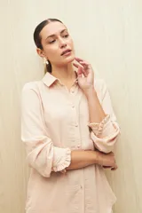 Camisa blanca de manga larga con textura sutil y caída fluida. Presenta cuello clásico, botones forrados a tono y puños con terminación fruncida.