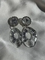 Aros colgantes con base redonda con strass plateado y dije circular irregular transparente con diseño plateado.