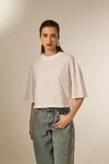 Remera blanca de manga 3/4, con cuello a la base y diseño holgado. Presenta un patrón de pequeños orificios y detalles de studs.
