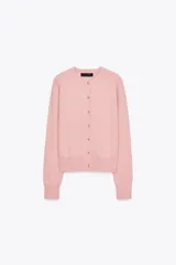 Chaqueta rosa de punto con cuello redondo y manga larga. Tiene hilo metalizado y cierre frontal con botones en relieve con forma de flor.