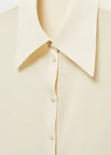 Camisa color crema de corte recto, con cuello camisero, cierre frontal con botones y mangas largas con puños abotonados.