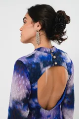Vestido largo con estampado abstracto en tonos azules, violetas y grises. Tiene cuello mao con abertura en forma de gota, mangas largas acampanadas con detalle de botón en los puños, espalda abierta, tajo frontal y flecos en el ruedo.
