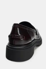 Zapato plano tipo mocasín color borgoña, con detalle de pasados en la parte delantera, copete subido y antifaz. Acabado en punta redondeada y suela track color negro.