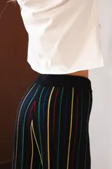 Pantalón negro con rayas verticales en amarillo, verde y rojo. Tejido con elástico en la cintura y lurex.