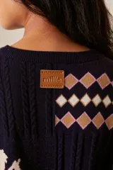 Cardigan azul marino de punto con cuello redondo y cierre frontal con botones. Presenta diseño con motivos geométricos en tonos beige, blanco y rosa, y un dibujo de un cupido en el pecho.