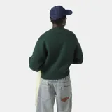 Sweater oversize color verde oscuro con cuello redondo y puños y dobladillo acanalados. Presenta el logo "EME STUDIOS" bordado en blanco en el pecho y la frase "curated by ben ice" debajo.