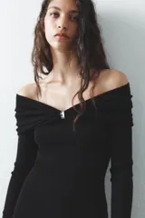 Vestido largo de punto negro con escote recto, hombros descubiertos, mangas largas y detalle de pieza metálica en el delantero.