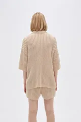 Remera de punto calado color beige, con cuello polo, mangas cortas y cierre frontal con botones.