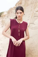 Vestido largo sin mangas color crudo, con cuello redondo y abertura frontal parcial con cierres dorados. Presenta un pequeño logo bordado en el pecho.