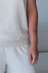 Musculosa color crudo, sin mangas, con cuello redondo y un pequeño bolsillo horizontal en el pecho. La prenda tiene un detalle de tejido o trenzado en la cintura.