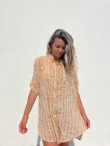 Camisa de manga corta color beige con bordados blancos verticales en forma de espiga. Presenta cuello mao y botones frontales.