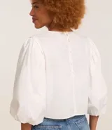 Blusa con cuerpo de tejido de ganchillo (crochet) bicolor azul y blanco con diseño floral, mangas largas abullonadas de tejido liso blanco y cuello redondo.