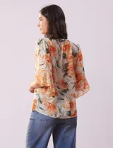 Blusa de gasa estampada con flores color naranja, marca Figueroa & Flower. Tiene cuello a la base, escote en V con lazo, abertura central con botones, delantera plisada y mangas 3/4 amplias.