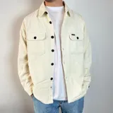 Sobrecamisa color crema de pana con cuello clásico, cierre frontal con botones negros, dos bolsillos de parche en el pecho con solapa abotonada y puños abotonados.