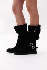 Bota de caña alta color negro, confeccionada en gamuza, con dos correas desmontables con hebillas metálicas.