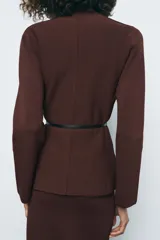 Chaqueta marrón de punto con cuello redondo y manga larga. Incluye cinturón fino negro con hebilla circular.