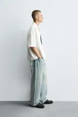 Camisa relaxed fit color blanco crudo, confeccionada en tejido de algodón con estructura. Cuello bowling y manga corta. Estampado frontal con la frase "ONLY DUST IS FOREVER" en negro. Cierre frontal de botonadura.