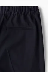 Pantalón tobillero azul marino de sarga suave con cintura elástica y cordón ajustable. Tiene bolsillos laterales y traseros ribeteados, piernas con pliegues cosidos y doblez en el bajo.