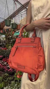 Mochila bandolera color marrón con herrajes color peltre. Tiene un compartimento principal amplio con cierre, un bolsillo frontal con cierre y dos bolsillos laterales abiertos. Incluye correa ajustable para usar al hombro o cruzada.