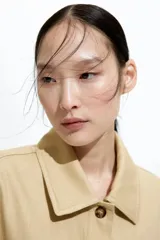 Campera color beige de sarga de algodón, con cuello, botones al frente y canesú en la espalda. Tiene hombros caídos, bolsillos superiores de parche, bolsillos insertados al frente y puños abotonados.
