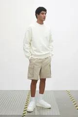 Short color beige de tejido grueso de algodón, con corte estándar, cintura elástica con cordón ajustable, bolsillos al bies y bolsillos de solapa con cierre autoadherente en las piernas y atrás.