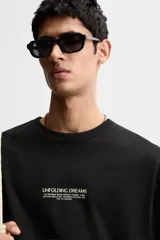 Camiseta negra de corte holgado con cuello redondo y mangas cortas. Estampado frontal con la frase "Unfolding Dreams" en letras blancas.