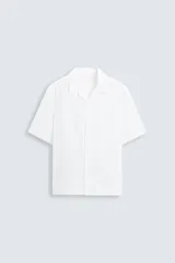 Camisa blanca de lino, corte relaxed fit, con cuello bowling, manga corta, bajo con aberturas laterales y cierre frontal de botonadura.