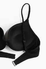 Top de bikini negro con textura acanalada, copas preformadas con relleno push-up, breteles finos ajustables y cierre de gancho en la espalda.