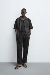 Pantalón negro de corte amplio, con textura acanalada, cintura elástica ajustable con cordón, bolsillos laterales y traseros de vivo.