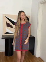 Vestido corto tejido en jacquard de algodón, con diseño a cuadros en tonos azul y marrón, cuello redondo con ribete rojo y cierre frontal con botones.