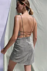 Vestido corto plateado metalizado con escote en V profundo, breteles finos, aberturas en la cintura y espalda descubierta.