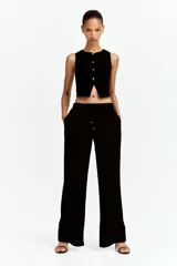 Pantalón negro de piernas anchas con bolsillos laterales, cintura elástica y cordón de ajuste con cuentas decorativas en los extremos.