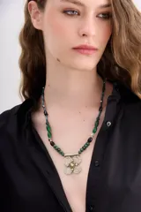 Collar de 50 cm de largo con cuentas de vidrio verdes y negras de diferentes formas y tamaños. Dije central metálico con forma de flor de cuatro pétalos color crema y centro dorado.