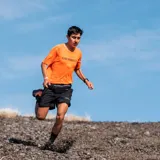 Remera deportiva naranja de poliéster y spandex, con logo Merrell estampado en el pecho.
