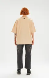 Remera color beige de corte crop y calce oversize, con hombros caídos y cuello redondo.