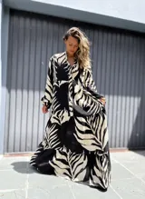 Vestido largo de manga larga, con cuello camisero y estampado de hojas tropicales en blanco y negro. El diseño presenta un corte amplio con volados en la falda.