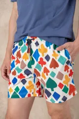 Short de baño azul vibrante con estampado repetitivo de cruces pequeñas en blanco y rojo. Presenta cintura elástica fruncida y cordón de ajuste trenzado en color coral con puntas de neón verde lima.