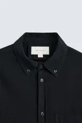 Camisa azul de algodón con textura chambray, corte regular fit, cuello abotonado, manga larga con puños abotonados, bolsillo de parche en el pecho y cierre frontal con botones.