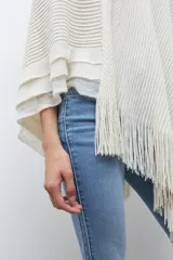 Capa tejida color negro, con cuello redondo, diseño de punto y detalles de lentejuelas. Presenta flecos en el dobladillo.