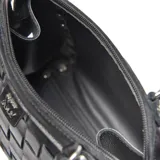 Cartera tipo baúl pequeña de cuero negro, con cuerpo tejido en patrón de cuadros (intrecciato) y tachas metálicas redondas en los bordes. Posee doble asa superior y correa ajustable para llevar al hombro o cruzada.