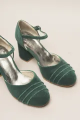 Zapato de tacón de terciopelo verde con correa al tobillo, punta redondeada y tacón cuadrado.