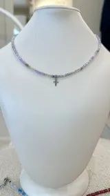 Collar de cristalitos facetados en tonos lila, celeste y plateado, con dije de cruz en acero plateado. Cierre de acero.
