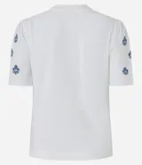 Remera blanca de algodón con cuello redondo, mangas cortas abullonadas y pequeños bordados florales azules en las mangas.
