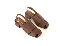 Sandalia de cuero color marrón con punta cuadrada y tiras anchas entrecruzadas. Tiene talón abierto con pulsera ajustable y hebilla metálica. El taco es ancho y mide 4 cm.