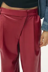 Pantalón de cuero sintético color bordó, de tiro medio, corte recto y cintura cruzada con trabillas. Cuenta con bolsillos laterales, pinzas delanteras y cierre frontal con cremallera, botón y gancho metálico.