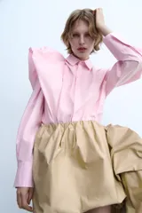 Camisa de popelín rosa de algodón, con cuello solapa, manga larga con puños plisados y volumen en un hombro. Cierre frontal con botones ocultos.