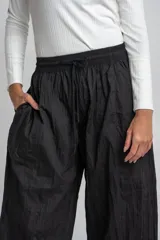 Pantalón negro de tela arrugada, corte ancho y cintura elastizada con cordón de ajuste.