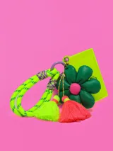 Llavero con cordón trenzado verde neón, detalles en violeta y dijes colgantes: flor verde con centro rosa, borla verde neón y borla fucsia. Incluye tarjetero de plástico rígido color verde neón.