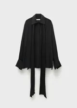 Camisa negra de tejido fluido semitransparente con lazo en el cuello, mangas largas con puños abotonados, diseño recto, cuello camisero, bajo con aberturas laterales y cierre delantero con botones.
