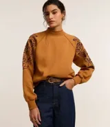 Sweater color ocre con cuello alto y mangas largas con sisas raglán. El sweater tiene bordados de flores en los laterales de las mangas.